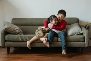 Two happy kids hugging and laughing while sitting on a couch in a cozy living room setting.
